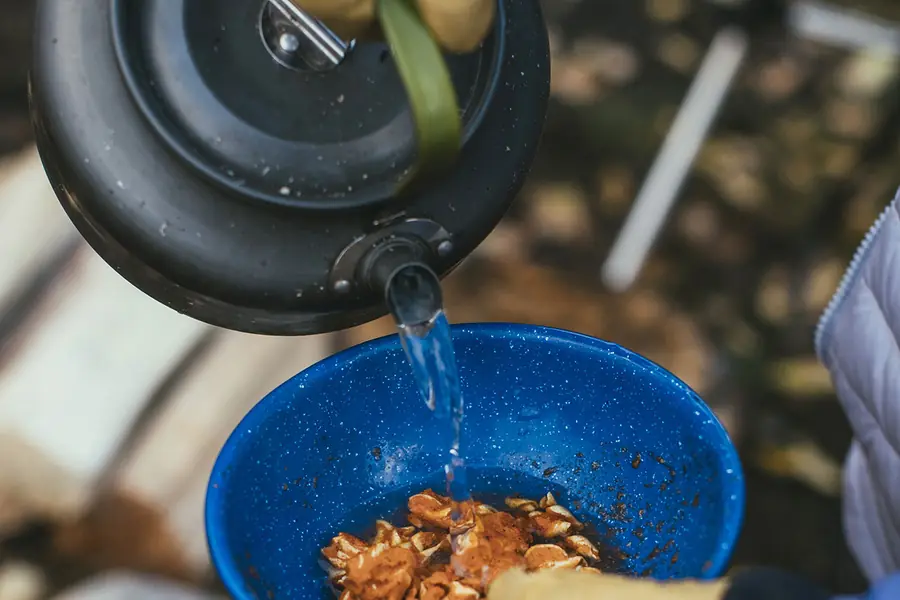 Kettle pouring hot water into a bowl of freeze dried food at a campsite
